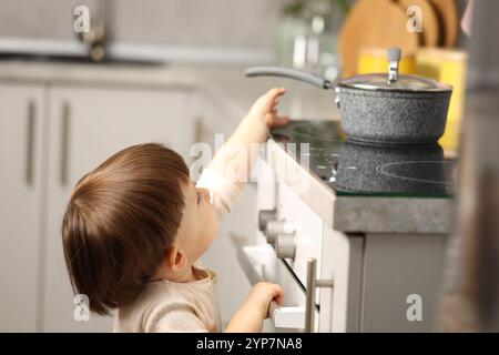 Bambino che gioca con la pentola su un fornello in cucina. Situazione pericolosa Foto Stock