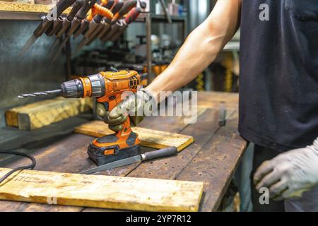 Primo piano di un operatore che indossa guanti protettivi utilizzando un trapano elettrico in fabbrica Foto Stock