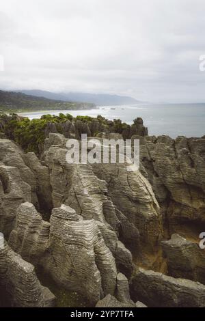 Formazioni rocciose ruvide su una costa nebbiosa con vista sul mare e sulla lontana linea dell'orizzonte, West Coast, nuova Zelanda, Oceania Foto Stock