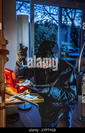 Symbolbild Wohnungseinbruch, Täter ist von der Gartenseite Her, in eine Wohnung eingedrungen und sucht nach Beute, bricht eine Geldkassette auf, findet Wertgegenstände, Geld, Einbrecher *** immagine simbolica del furto, l'esecutore ha rotto in un appartamento dal lato del giardino e sta cercando bottino, rompe apre una cassa, trova oggetti di valore, denaro Foto Stock