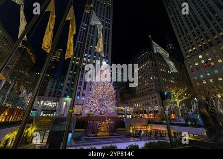 L'iconico albero di Natale del Rockefeller Center splendidamente illuminato con luci colorate, circondato da bandiere e architettura urbana, catturato di notte. Il Foto Stock