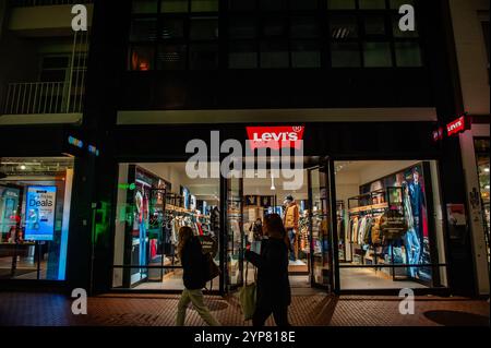 Nijmegen, Paesi Bassi. 28 novembre 2024. Le persone sono viste passare di fronte al negozio "Levis". L'unico giorno della settimana (giovedì) che i negozi aprono fino alle 21:00, erano già pronti con le offerte del Black Friday. Circa un terzo dei residenti olandesi ritardano gli acquisti per ottenere un affare migliore il Black Friday. Il Black Friday sta diventando sempre più il momento di passare a Internet e ai servizi di streaming. Credito: SOPA Images Limited/Alamy Live News Foto Stock