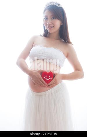 Donna incinta in abito che tiene il cuore imbottito Foto Stock