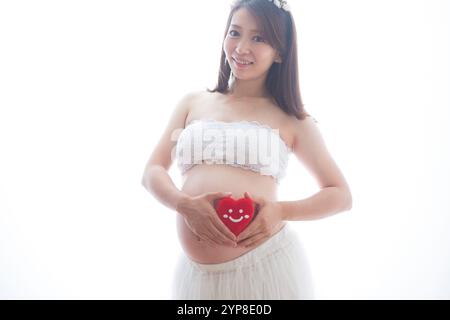 Donna incinta in abito che tiene il cuore imbottito Foto Stock