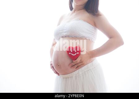 Donna incinta in abito che tiene il cuore imbottito Foto Stock