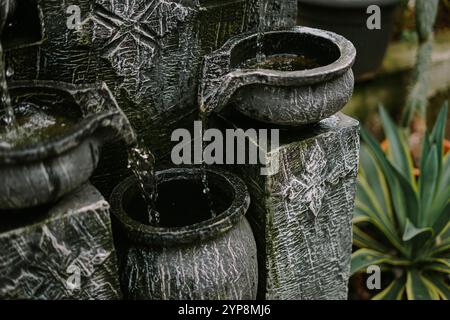 Un piccolo giardino decorativo con una fontana unica in pietra nera, circondato da piante vibranti, cactus e ciottoli bianchi, che creano un ambiente tranquillo e tranquillo Foto Stock