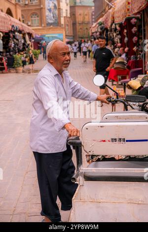 Kashgar, Cina - 17 LUGLIO 2022: Uomo uiguro circondato da tradizionali negozi di cappelli uiguri in un mercato locale nella vecchia Kashgar Foto Stock