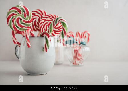 Canne di caramelle natalizie, lecca lecca e marshmallow in una tazza su sfondo chiaro Foto Stock
