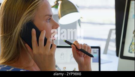 Vista laterale della stilista caucasica che parla al telefono cellulare in ufficio Foto Stock