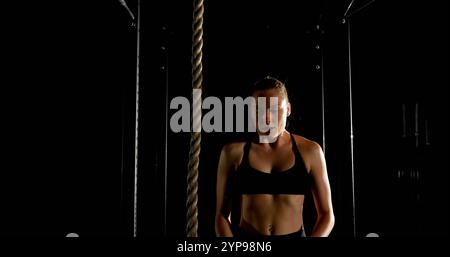 Vista frontale dell'atleta caucasica che si arrampica su una corda nella sala fitness Foto Stock