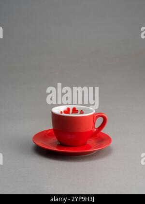 Natura morta di una tazza di caffè rossa con decorazioni a forma di cuore, su sfondo grigio Foto Stock