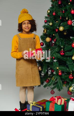 Una ragazza in un intimo abito regala un regalo accanto a un albero di Natale decorato e scintillante. Foto Stock