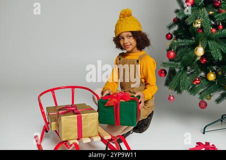 Il piccolo sorride mentre organizza regali colorati vicino a un albero di Natale splendidamente decorato. Foto Stock