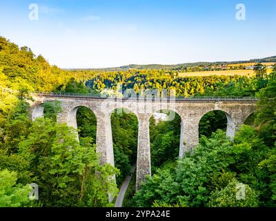 Il ponte ferroviario in pietra di Zampach si estende su alberi lussureggianti, mostrando imponenti archi in pietra contro un cielo limpido, situato nella panoramica campagna ceca. Foto Stock