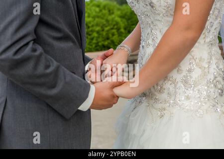 Sposa e sposo che si tengono per mano il primo piano il giorno delle nozze: Un momento elegante e romantico Foto Stock