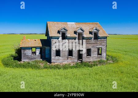 Una grande e vecchia casa si trova in un campo d'erba. La casa è in stato di abbandono, con molte finestre rotte e un tetto mancante. L'erba Foto Stock