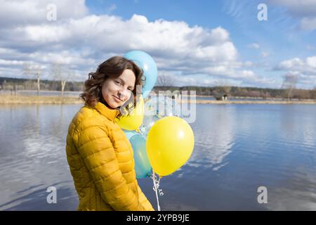 ritratto di donna sullo sfondo del lago nelle giornate di sole, con palloncini gialli e blu. identità nazionale, fiducia nella vittoria. Giorno dell'indipendenza di Ukra Foto Stock