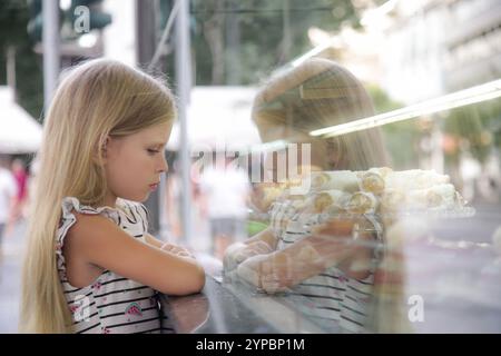 Piccola scontrosa e triste che guarda la vetrina di un negozio di dolci Foto Stock