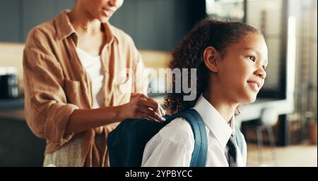Mamma, ragazza e felice con lo zaino in casa per prepararsi o prepararsi per l'istruzione elementare. Appartamento, persone e genitore con bambino in uniforme per prima Foto Stock