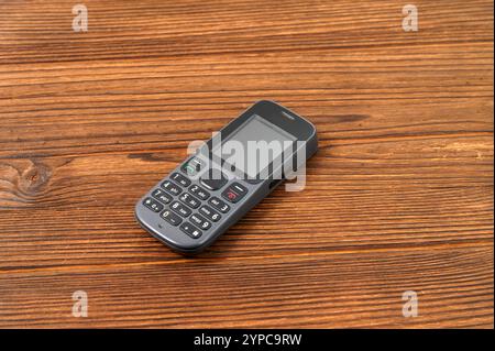 Questa immagine mostra un semplice telefono cellulare classico appoggiato su una superficie in legno. Foto Stock