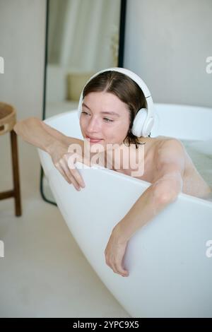 Ripresa verticale di una donna rilassata che ascolta la musica mentre fa il bagno, si diverte con la procedura Foto Stock