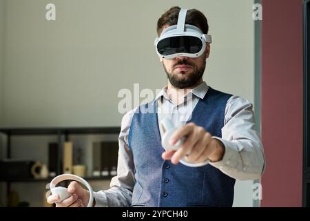 Giovane dipendente di sesso maschile che punta sullo schermo virtuale interattivo durante la presentazione o lo studio dei dati in ufficio Foto Stock