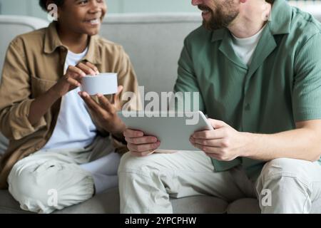 Sorridendo persone diverse che interagiscono con un tablet e un altoparlante intelligente, coinvolti in una vivace discussione sulle tendenze tecnologiche moderne Foto Stock