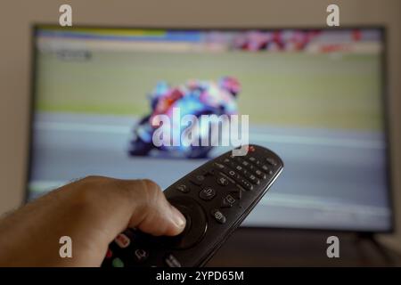 11 maggio 2024, Brasile. In questa illustrazione fotografica, una mano che tiene un telecomando TV davanti alla a che trasmette una gara motociclistica in TV Foto Stock