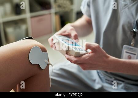 Esecuzione della terapia di stimolazione elettrica sul braccio del paziente in ambiente clinico, utilizzando un dispositivo portatile ed un elettrodo collegati alla cute del paziente. L'immagine mostra una vista ravvicinata del processo di trattamento Foto Stock