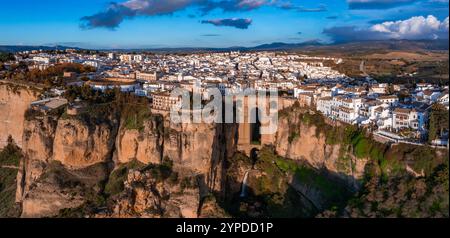 L'immagine cattura il ponte Puente Nuevo di Ronda che si estende su una profonda gola, con edifici imbiancati sulle scogliere e la campagna sullo sfondo al tramonto Foto Stock