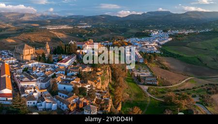 Ronda, in Spagna, vista dall'alto al tramonto, presenta il ponte Puente Nuevo, gli edifici imbiancati su una scogliera e le montagne della Sierra de las Nieves. Foto Stock