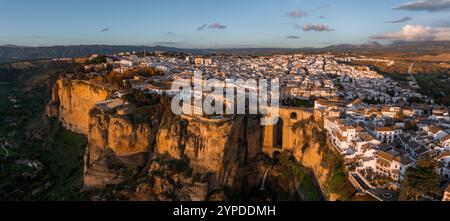 Vista aerea di Ronda, Spagna al tramonto, con il ponte Puente Nuevo su una profonda gola, con edifici imbiancati e colline ondulate nella ba Foto Stock