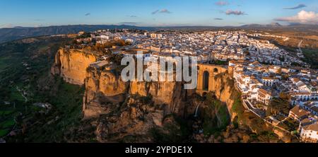 Ronda, Spagna, è visibile dall'alto al tramonto, con il ponte Puente Nuevo su una profonda gola. Sono visibili edifici imbiancati e terreni accidentati. Foto Stock