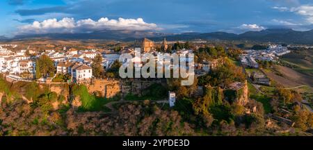 Ronda, Spagna, è visibile dall'alto al tramonto, con il ponte Puente Nuevo. La città si trova su una scogliera con colline ondulate e montagne nel backgro Foto Stock