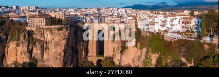 Ronda, Spagna, è vista dall'alto, con il ponte Puente Nuevo sulla gola di El Tajo. Gli edifici imbiancati fiancheggiano le scogliere, illuminate dai setti Foto Stock