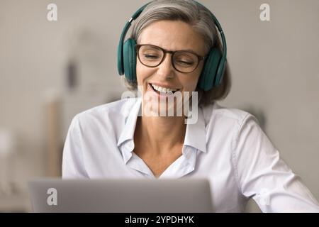 Una donna positiva felice piuttosto matura con gli occhiali seduti al computer portatile Foto Stock