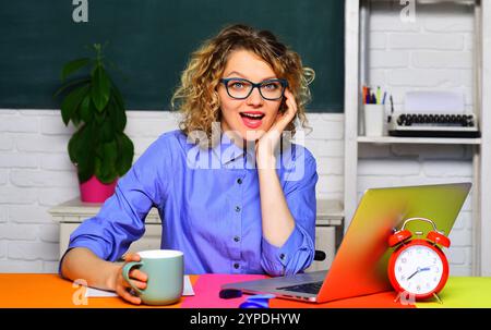 Professoressa sorridente o professoressa universitaria seduta alla scrivania in classe e pausa caffè. Apprendimento, istruzione e conoscenza. Insegnante di scuola Foto Stock