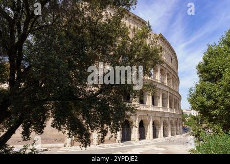 Il grande Colosseo Romano, noto anche come Anfiteatro Flavio, delimitato da alberi a Roma, in Italia, in una splendida giornata con un cielo blu profondo Foto Stock