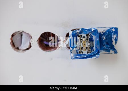 Primo piano dell'installazione di prese elettriche non completate in una parete bianca con nastro protettivo blu durante la ristrutturazione della casa Foto Stock