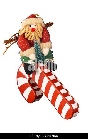 Bambola di straccio Babbo Natale regge un albero di Natale e scivola su un gigantesco bastone da zucchero a righe rosse bianche. Indossa un cappello e vestiti rossi e verdi. Divertente Foto Stock