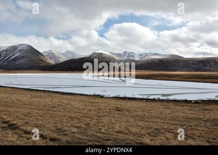 Congelato dopo le prime gelate, un enorme lago adagiato nelle steppe ai piedi delle montagne innevate in una soleggiata giornata autunnale. Foto Stock