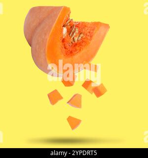 Pezzi di zucca cruda fresca che cadono su sfondo giallo Foto Stock