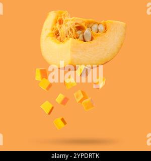 Pezzi di zucca cruda fresca che cadono su sfondo arancione Foto Stock