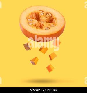 Pezzi di zucca cruda fresca che cadono su sfondo dorato Foto Stock