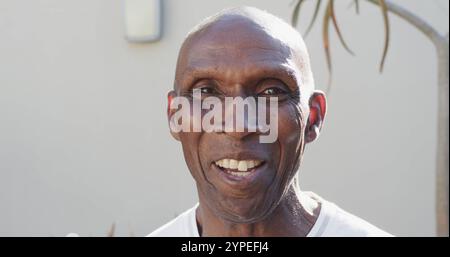 Ritratto di un uomo afroamericano felice e inalterato davanti al muro e alle piante, al rallentatore Foto Stock