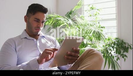 Vista frontale di un uomo birazziale che lavora in un ufficio creativo e utilizza un tablet Foto Stock