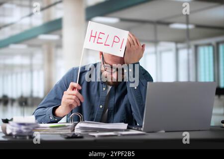 Contabile sovraccaricato con un cartello di aiuto mentre lavora alla scrivania in ufficio Foto Stock