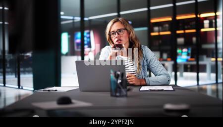 Donna d'affari professionista che utilizza l'app per smartphone per le chiamate client in un ufficio moderno con laptop e sorridente Foto Stock