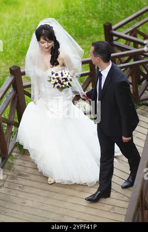 Coppia di sposi che si tiene per mano e scende le scale di legno in un parco, celebrando il loro amore e impegno Foto Stock