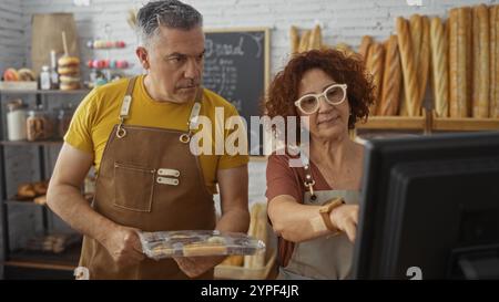 Fornai professionisti, uomo e donna insieme in una panetteria che utilizza un computer al chiuso. Foto Stock